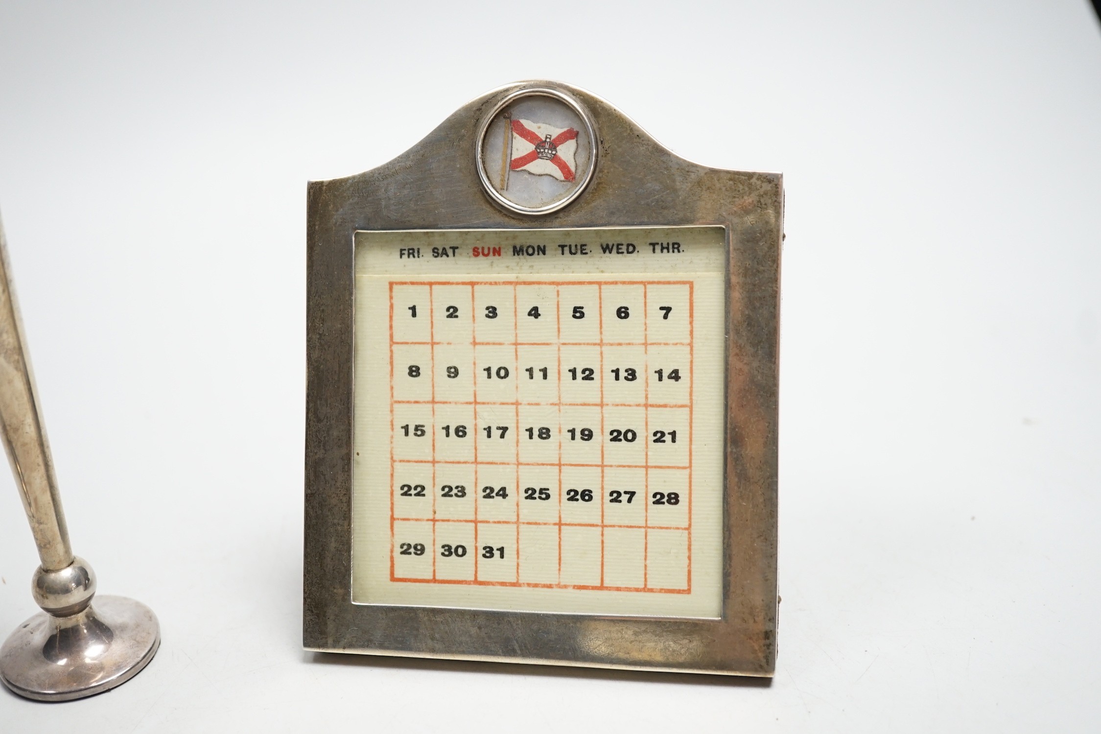 A white metal mounted desk calendar, with inset flag and two small silver mounted vases.